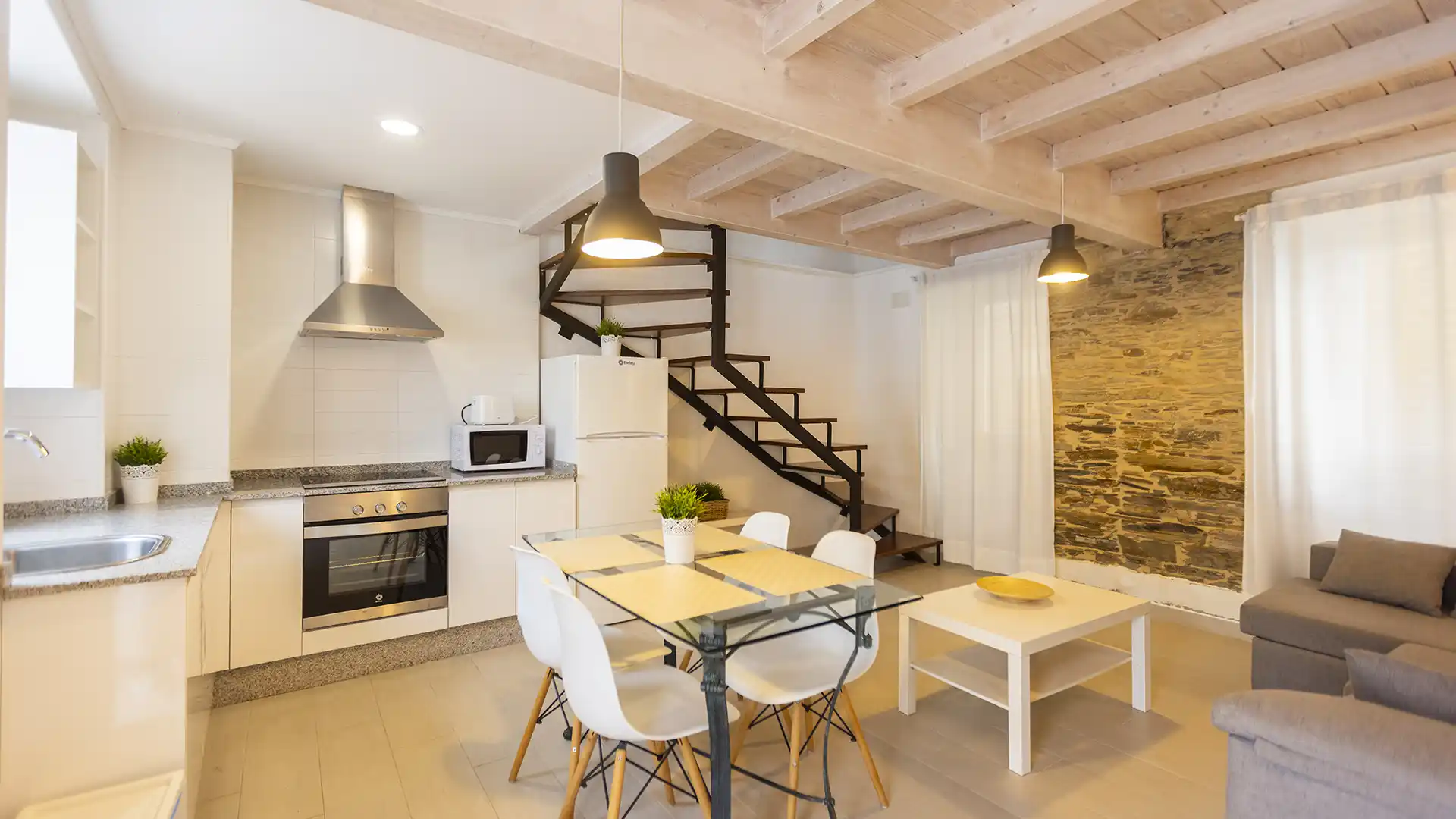 Cocina blanca, mesa de comedor y escalera de madera en el salón de un apartamento de Apartagal
