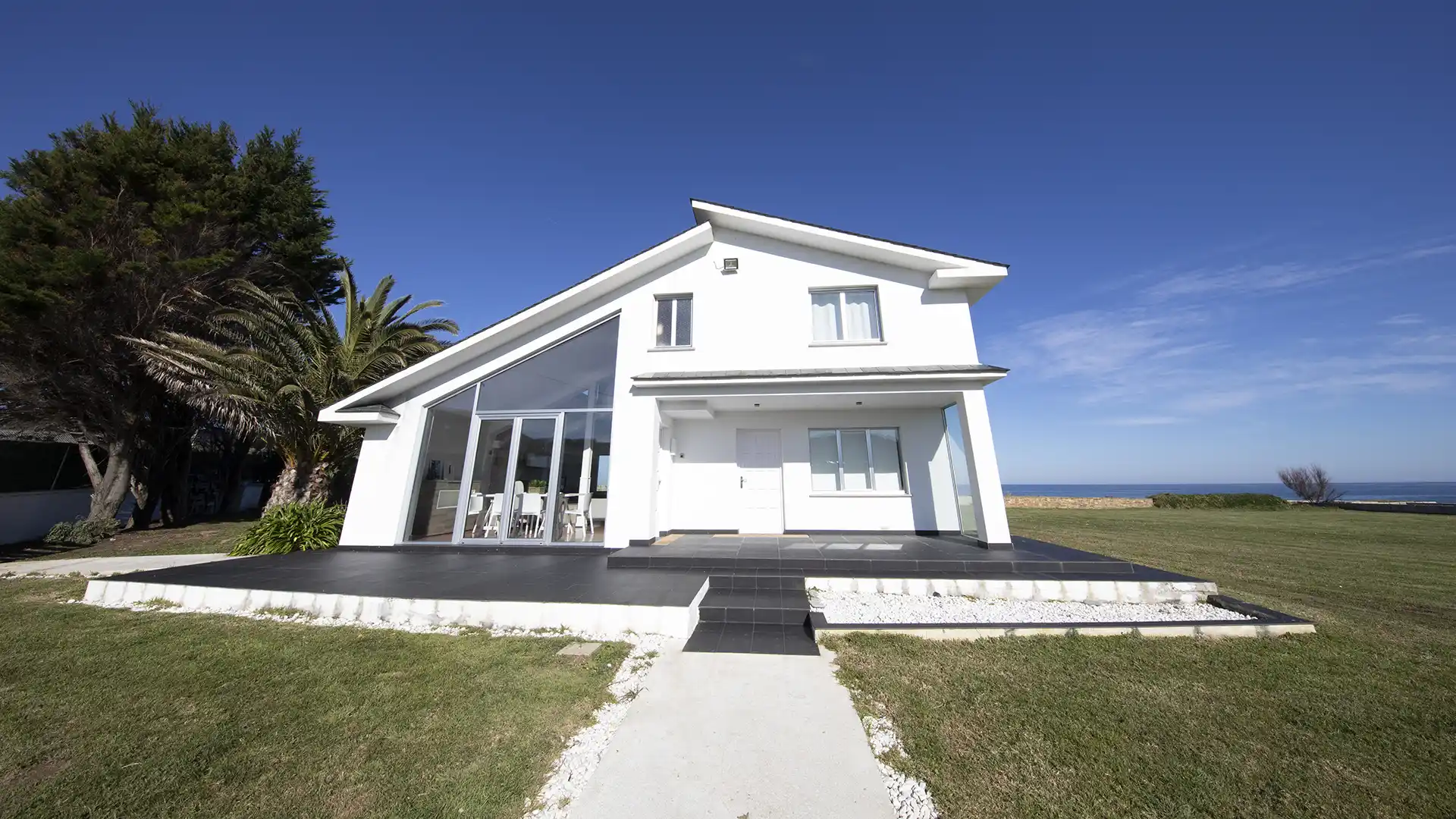 Casa blanca de dos plantas con amplios ventanales, jardín y vistas al mar en la costa de Foz