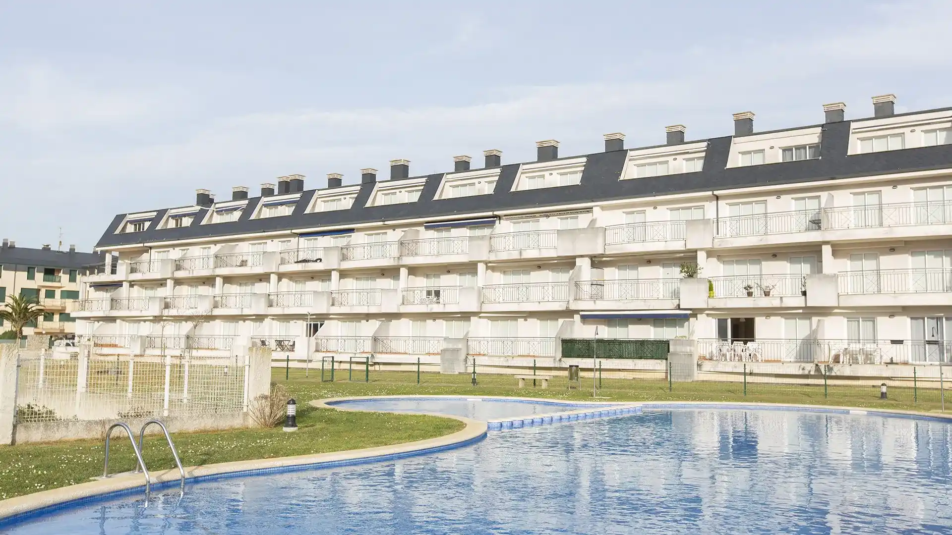 Fachada de apartamentos con balcones y buhardillas junto a una piscina comunitaria y césped en Barreiros