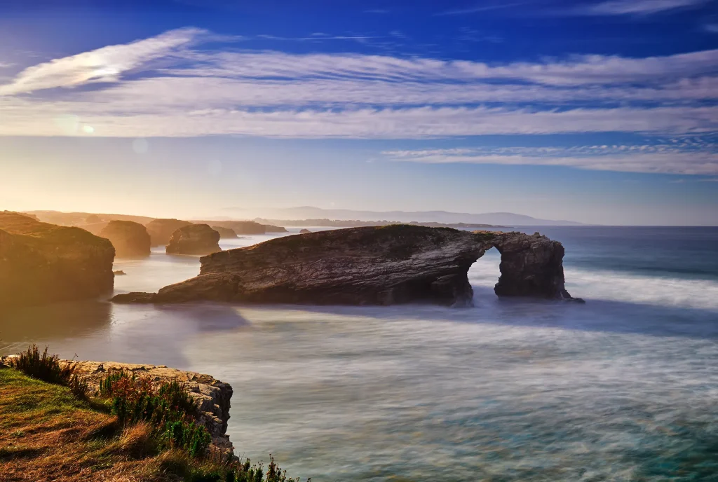 Arco de roca natural en la playa de las Catedrales con acantilados y mar en calma al atardecer