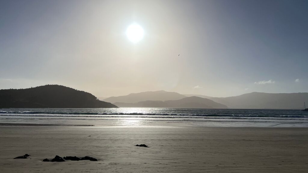 Playa de Espasante con el sol reflejándose en el mar en calma y montañas al fondo