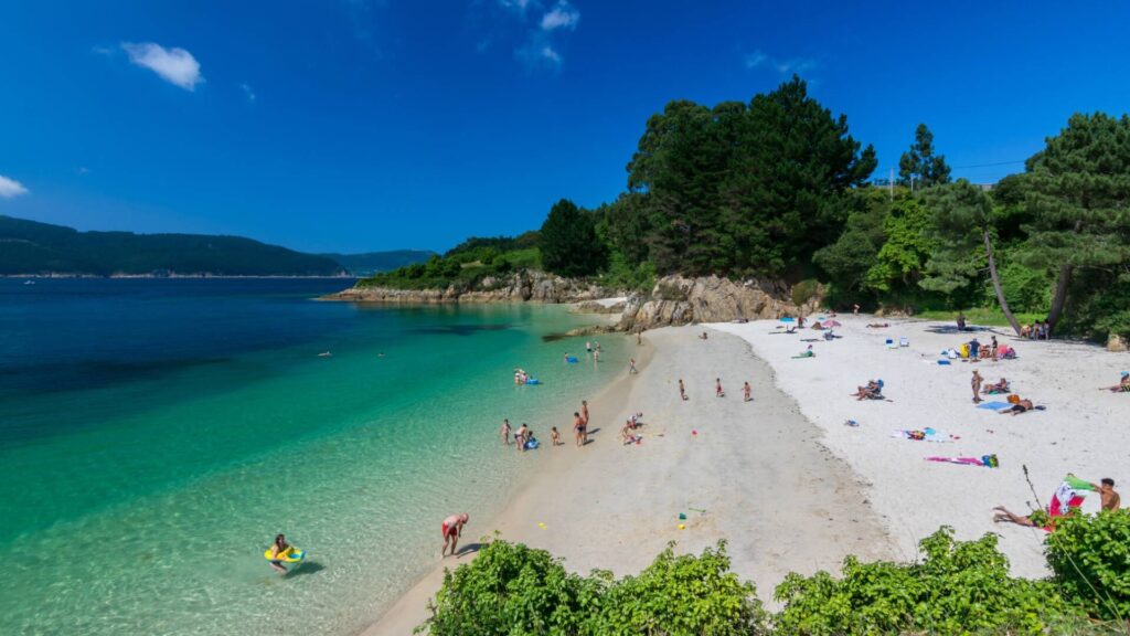 Cala de arena blanca y agua turquesa con pinos y rocas de granito en la Mariña Lucense